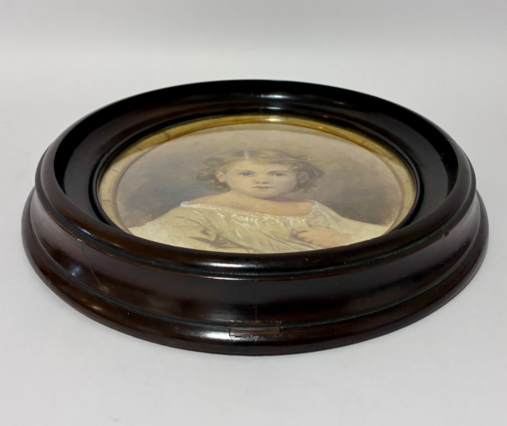 An oval Edwardian watercolour portrait depicting a young child with blonde curls, set inside a dark wooden frame with a gilt inner trim. View VI