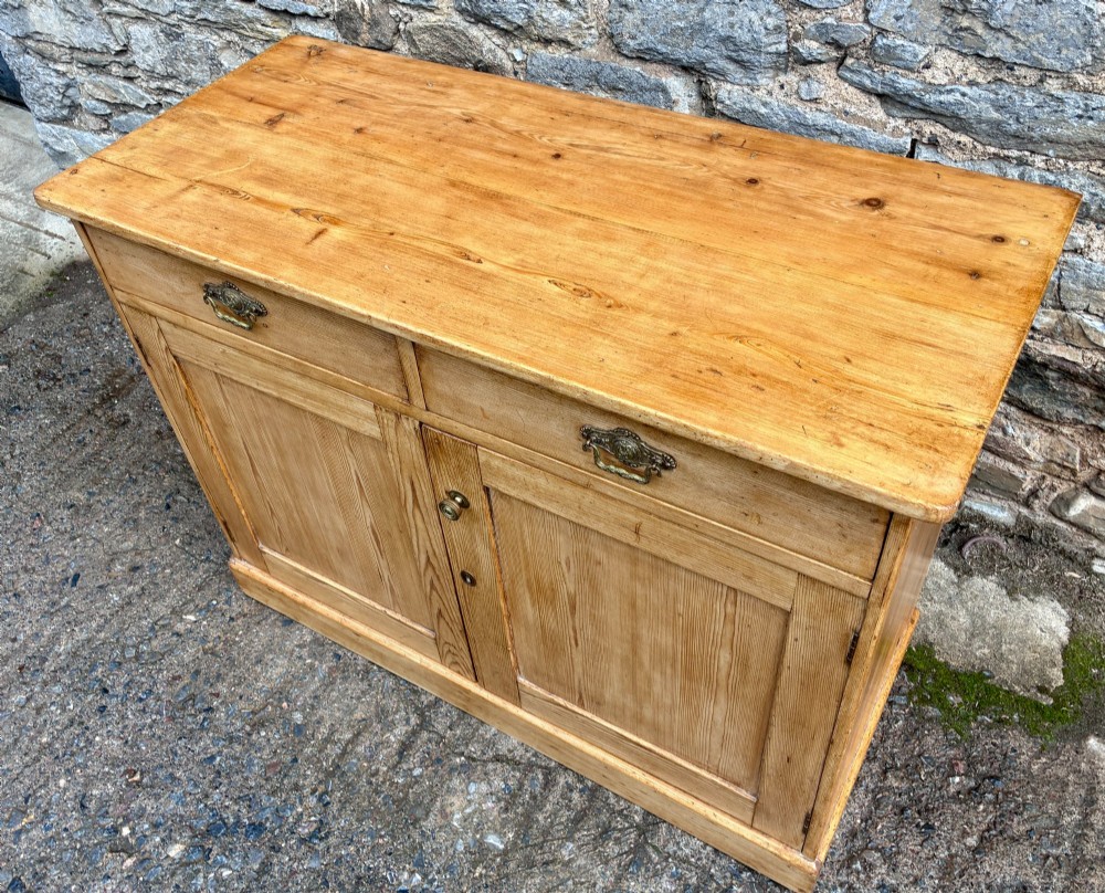 A nineteenth-century stripped pine sideboard featuring two upper drawers with ornate brass handles above two panelled cupboard doors on a solid plinth base. View VIII