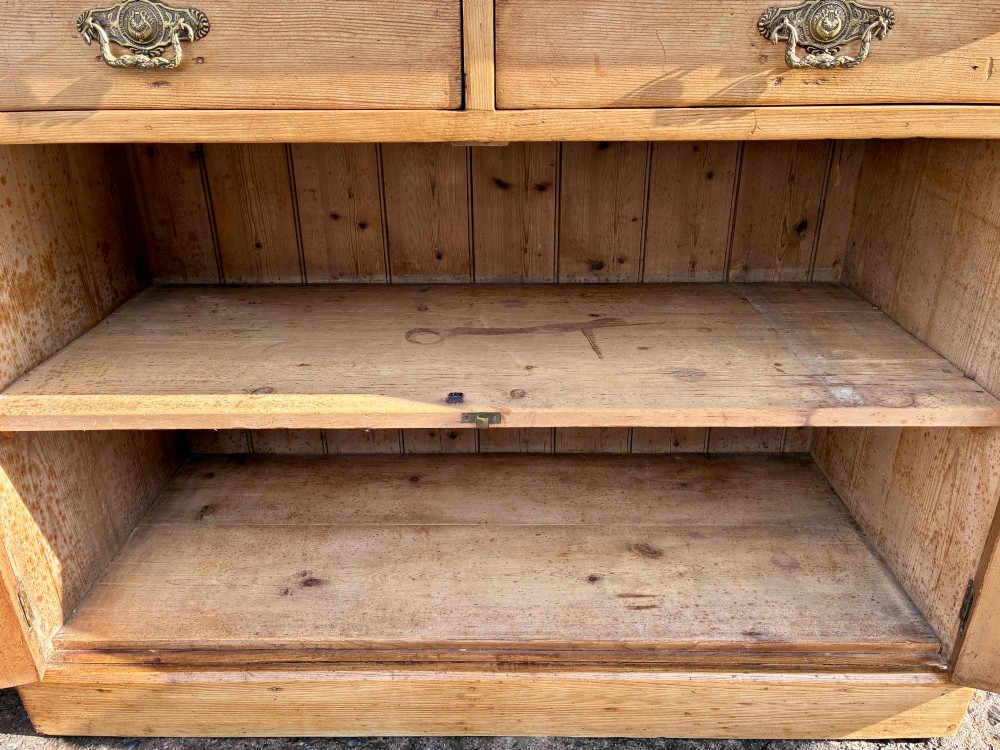 A nineteenth-century stripped pine sideboard featuring two upper drawers with ornate brass handles above two panelled cupboard doors on a solid plinth base. View XII