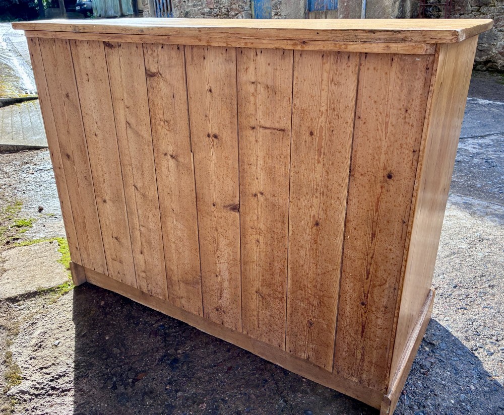 A nineteenth-century stripped pine sideboard featuring two upper drawers with ornate brass handles above two panelled cupboard doors on a solid plinth base. View XIV