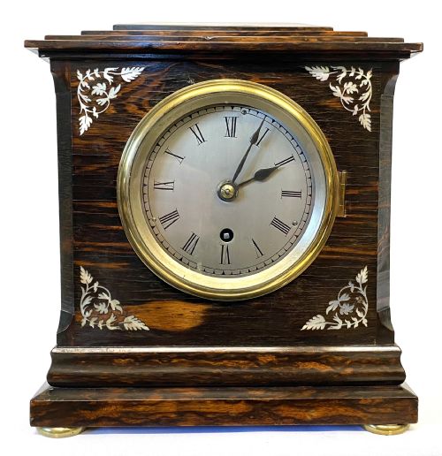fig 1. An antique coromandel wood mantel clock featuring mother-of-pearl corner inlays, a round brass bezel, and a silvered dial with Roman numerals.