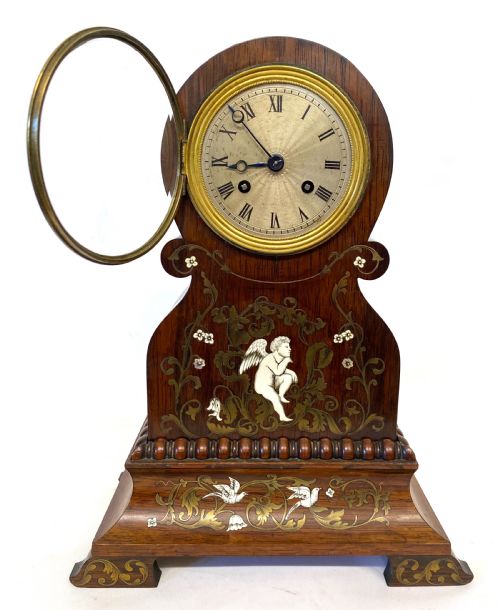 fig 2. An antique French rosewood mantel clock featuring detailed brass foliage marquetry, bone cherub inlay, and a circular Roman numeral dial.