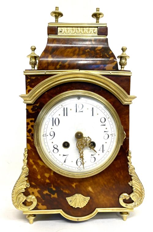 fig 1. An antique French mantel clock featuring tortoiseshell veneer, gilt bronze mounts, turned finials, and a white enamel dial with Arabic numerals.