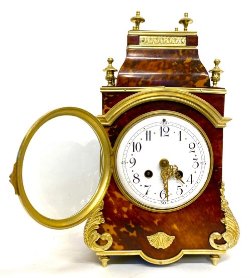 fig 2. An antique French mantel clock featuring tortoiseshell veneer, gilt bronze mounts, turned finials, and a white enamel dial with Arabic numerals.