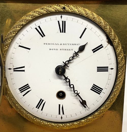 fig 2. An antique gilt bronze mantel clock featuring a white enamel dial alongside a standing Cupid figure holding an arrow, set upon a decorative gilded plinth base.