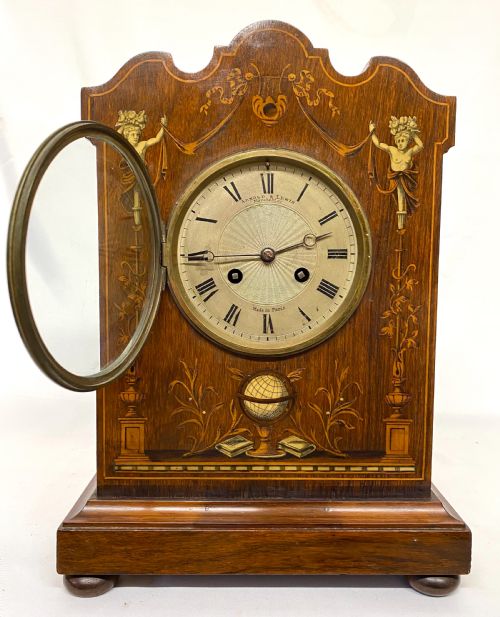 fig 2. An antique rosewood mantel clock featuring intricate marquetry inlays of figures, swags, and a globe surrounding a circular dial with Roman numerals.