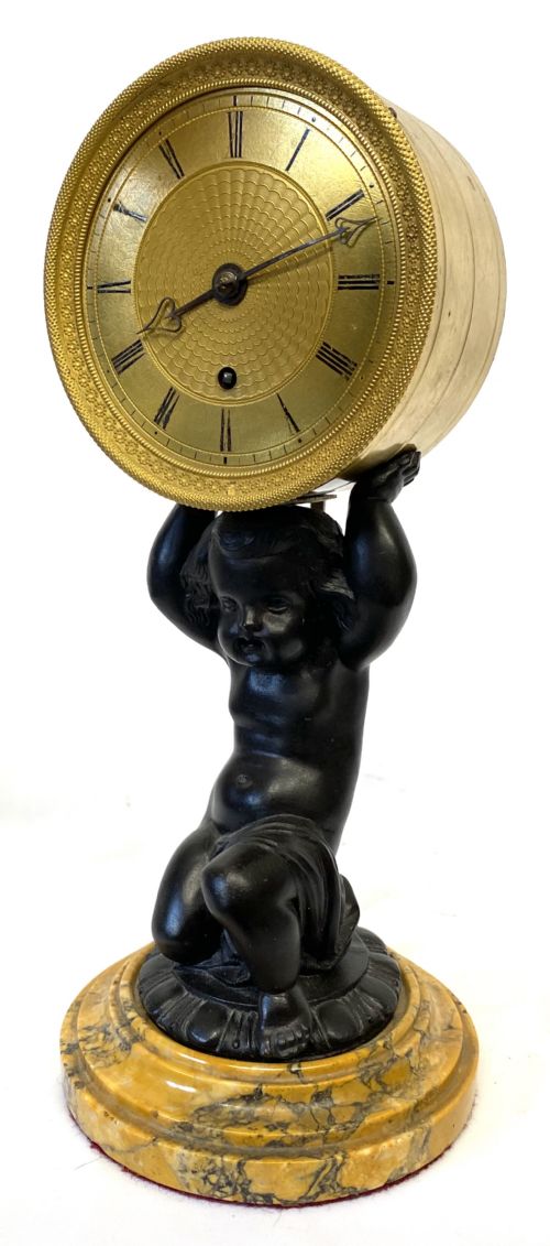 fig 1. An antique gilt brass and dark patinated bronze mantel clock depicting a kneeling cherub supporting a circular drum dial above a veined yellow marble base.