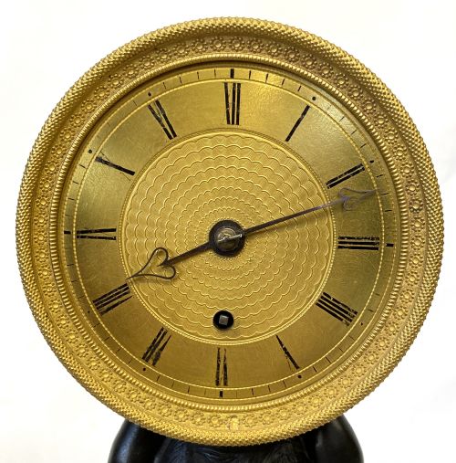 fig 3. An antique gilt brass and dark patinated bronze mantel clock depicting a kneeling cherub supporting a circular drum dial above a veined yellow marble base.