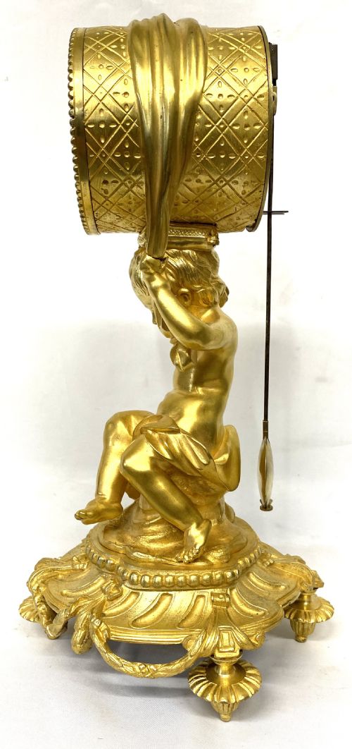 fig 1. A gilt bronze Victorian mantel clock featuring a sculpted cherub supporting a circular white enamel clock dial signed John Bennett London.