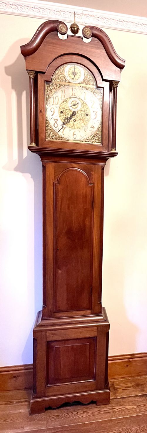fig 1. A mahogany longcase clock featuring a swan-neck pediment, brass arch dial with silvered chapter ring, fluted columns, and a shaped trunk door.