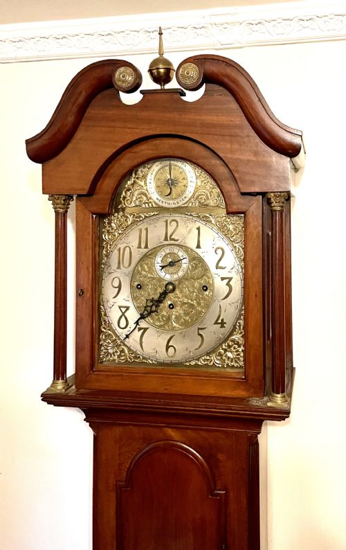 fig 3. A mahogany longcase clock featuring a swan-neck pediment, brass arch dial with silvered chapter ring, fluted columns, and a shaped trunk door.