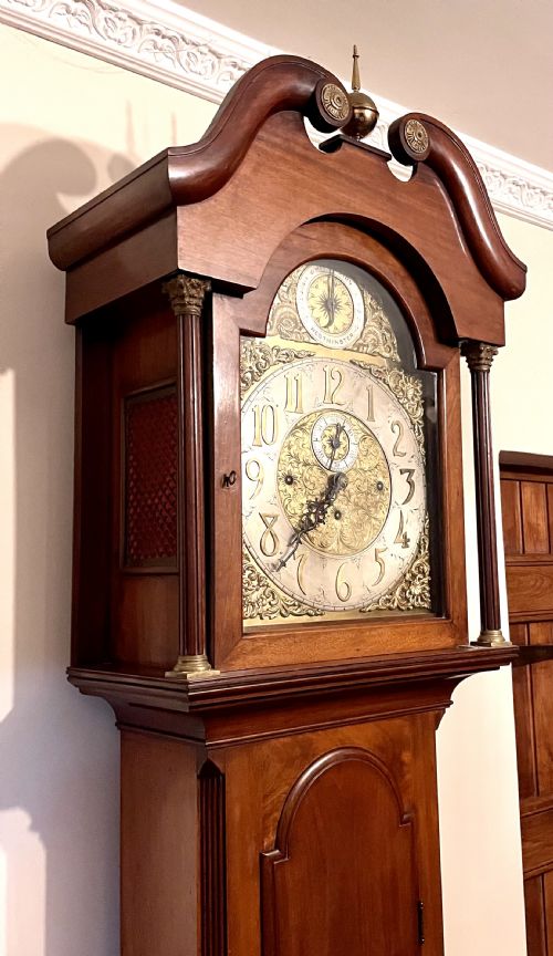 fig 4. A mahogany longcase clock featuring a swan-neck pediment, brass arch dial with silvered chapter ring, fluted columns, and a shaped trunk door.
