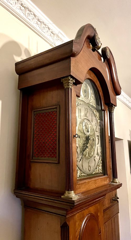 fig 5. A mahogany longcase clock featuring a swan-neck pediment, brass arch dial with silvered chapter ring, fluted columns, and a shaped trunk door.