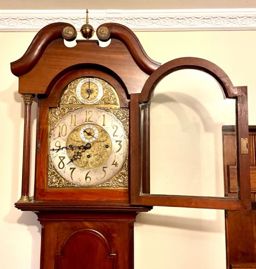 fig 6. A mahogany longcase clock featuring a swan-neck pediment, brass arch dial with silvered chapter ring, fluted columns, and a shaped trunk door.