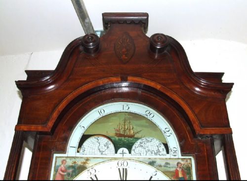 fig 5. An antique mahogany longcase grandfather clock featuring a painted arched dial with a moon phase indicator, swan neck pediment, and flame mahogany inlaid cabinet door.