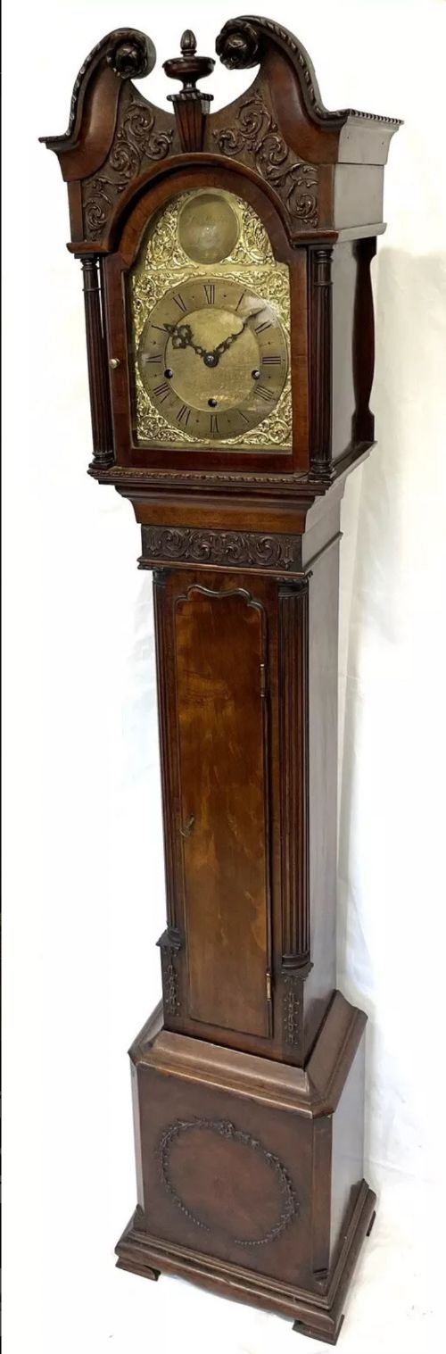 fig 1. An antique mahogany grandmother clock featuring a swan-neck pediment, carved scrollwork details, fluted columns, and an ornate brass dial with Roman numerals.