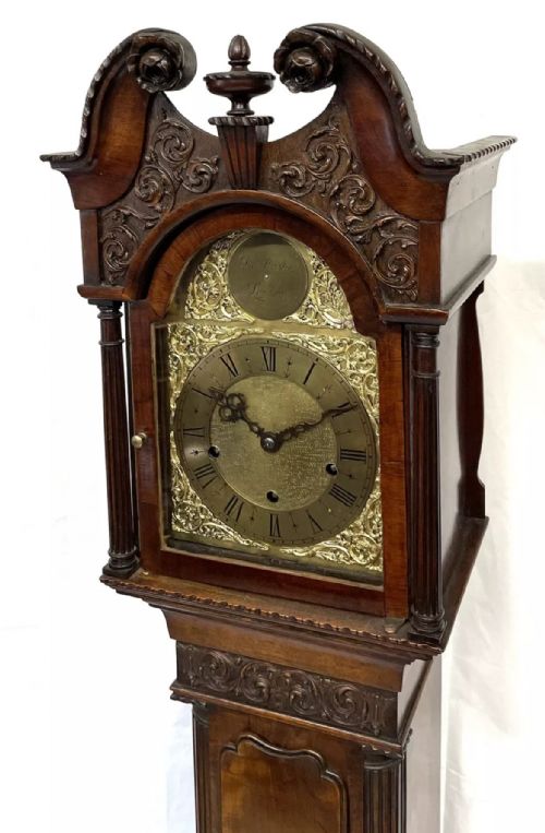 fig 4. An antique mahogany grandmother clock featuring a swan-neck pediment, carved scrollwork details, fluted columns, and an ornate brass dial with Roman numerals.