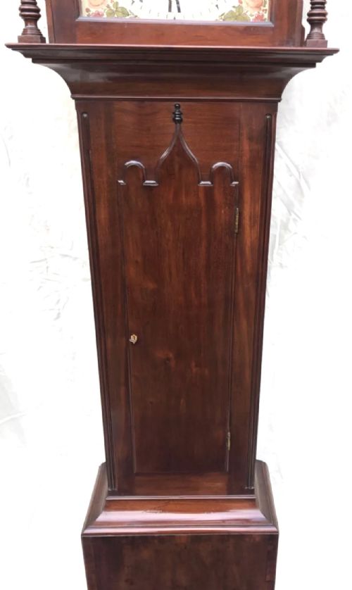 fig 6. An antique mahogany longcase clock featuring a swan-neck pediment, brass finials, a painted arch dial with a rocking seesaw automaton, and a gothic-arched trunk door.