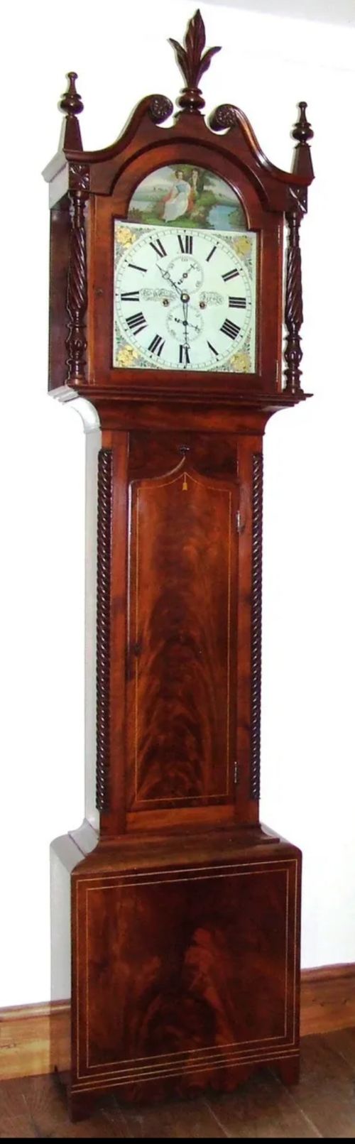 fig 1. An antique inlaid mahogany longcase clock featuring a swan-neck pediment with finials, a painted arch dial, and twisted side columns.