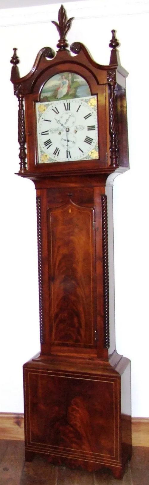 fig 2. An antique inlaid mahogany longcase clock featuring a swan-neck pediment with finials, a painted arch dial, and twisted side columns.
