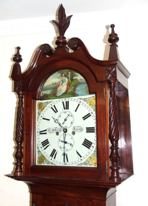 fig 3. An antique inlaid mahogany longcase clock featuring a swan-neck pediment with finials, a painted arch dial, and twisted side columns.