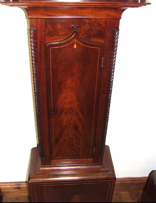 fig 7. An antique inlaid mahogany longcase clock featuring a swan-neck pediment with finials, a painted arch dial, and twisted side columns.