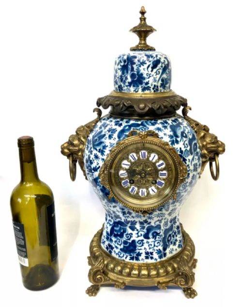 fig 1. A porcelain urn-shaped mantel clock decorated with blue and white floral patterns, featuring gilt bronze lion mask side handles and a cast metal scrolled base.