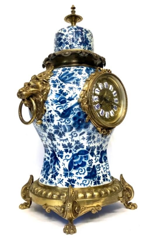 fig 2. A porcelain urn-shaped mantel clock decorated with blue and white floral patterns, featuring gilt bronze lion mask side handles and a cast metal scrolled base.
