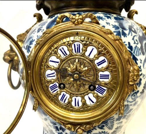 fig 3. A porcelain urn-shaped mantel clock decorated with blue and white floral patterns, featuring gilt bronze lion mask side handles and a cast metal scrolled base.