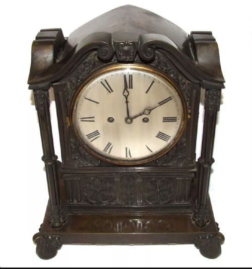 fig 1. A dark brown patinated bronze mantel clock featuring Gothic architectural columns, decorative relief carvings, scroll feet, and a silvered circular dial with Roman numerals.