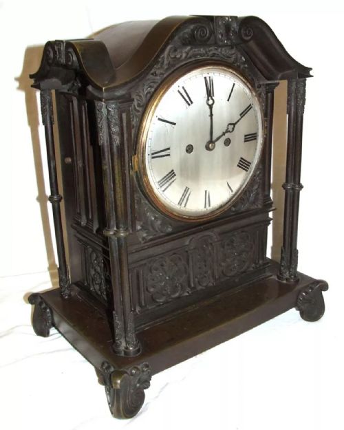 fig 2. A dark brown patinated bronze mantel clock featuring Gothic architectural columns, decorative relief carvings, scroll feet, and a silvered circular dial with Roman numerals.