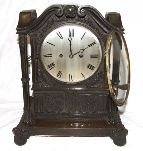 fig 3. A dark brown patinated bronze mantel clock featuring Gothic architectural columns, decorative relief carvings, scroll feet, and a silvered circular dial with Roman numerals.