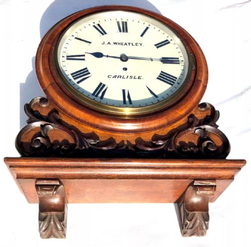 fig 3. Victorian mahogany circular fusee wall clock with carved scrollwork base and a white dial signed J. A. Wheatley Carlisle.