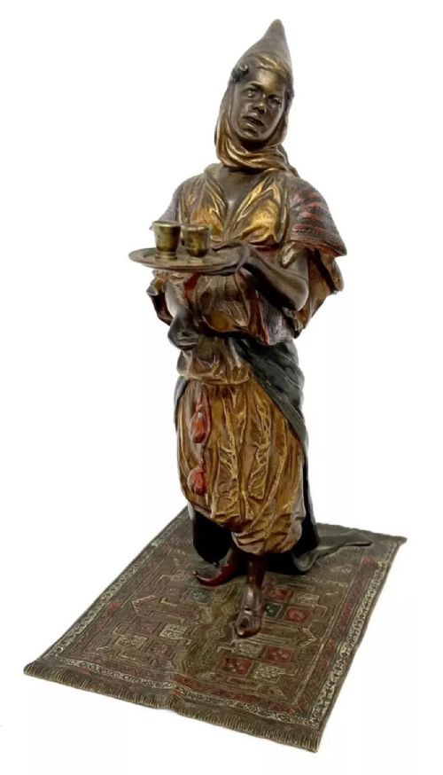 fig 1. An antique cold-painted bronze statuette depicting an Arab woman carrying a tea tray while standing on an engraved rug base.