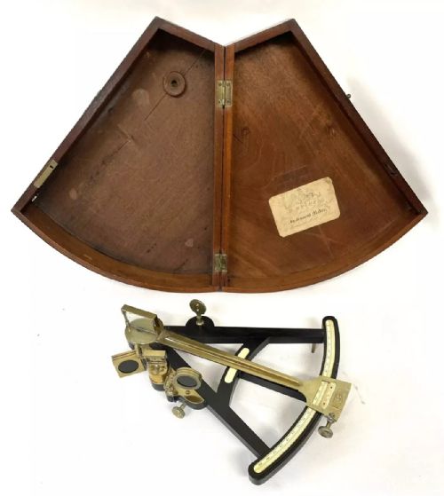 fig 1. An antique brass and ebony marine octant with an inlaid arc scale, set inside an open keystone-shaped mahogany carrying case with a paper maker label.