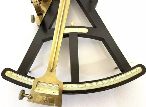 fig 4. An antique brass and ebony marine octant with an inlaid arc scale, set inside an open keystone-shaped mahogany carrying case with a paper maker label.