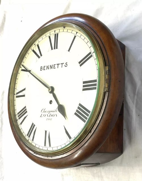 fig 3. An antique circular mahogany wall clock featuring an off-white dial with black Roman numerals, brass bezel, and Bennetts Cheapside London inscription.