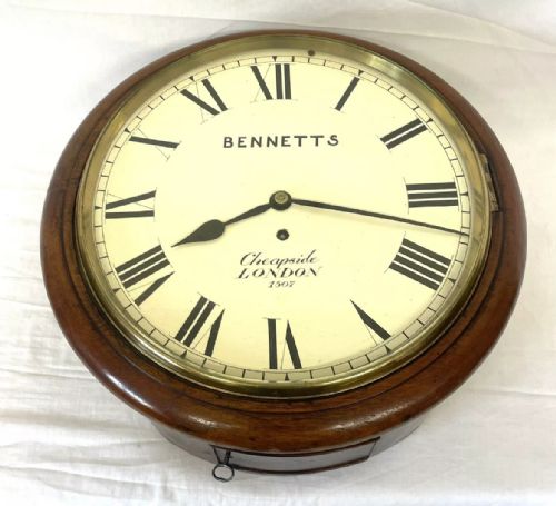 fig 4. An antique circular mahogany wall clock featuring an off-white dial with black Roman numerals, brass bezel, and Bennetts Cheapside London inscription.