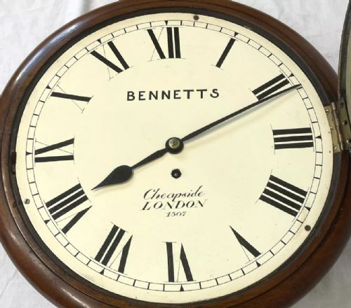 fig 6. An antique circular mahogany wall clock featuring an off-white dial with black Roman numerals, brass bezel, and Bennetts Cheapside London inscription.
