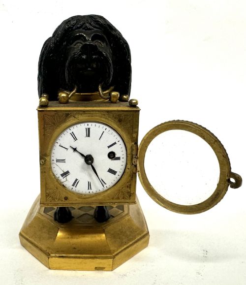 fig 1. A French gilt and patinated bronze timepiece featuring a standing dog figure holding a square glass clock case in its mouth on a gilded base.