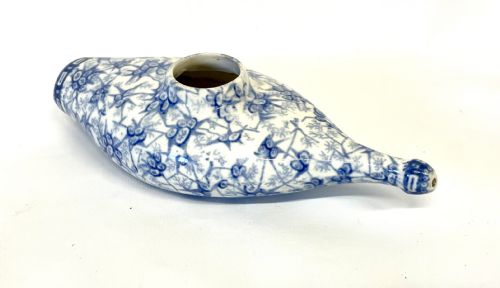 fig 1. A nineteenth-century ceramic baby feeding bottle decorated with blue and white floral transferware motifs, featuring a central circular opening and an elongated spout.