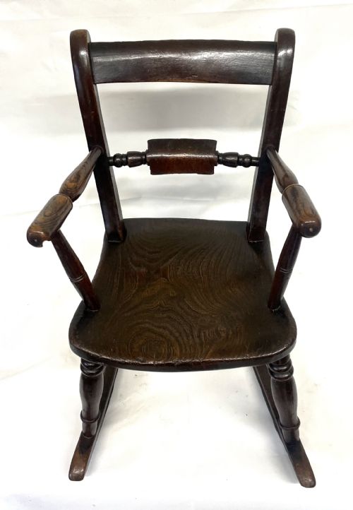 fig 2. A dark brown wooden childs or dolls rocking armchair featuring turned legs, curved armrests, and smooth wooden rockers.