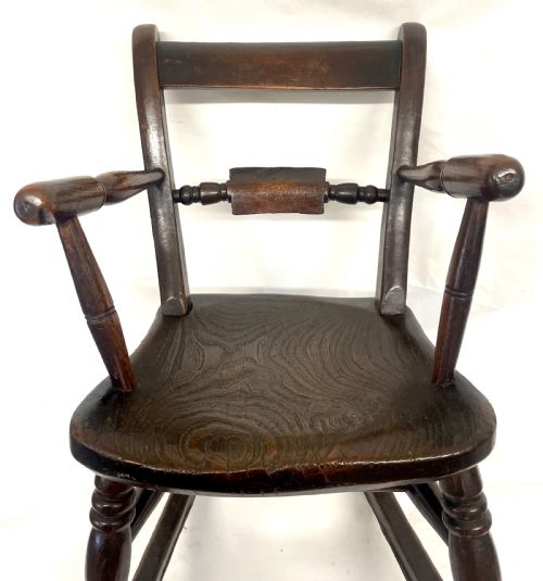 fig 3. A dark brown wooden childs or dolls rocking armchair featuring turned legs, curved armrests, and smooth wooden rockers.