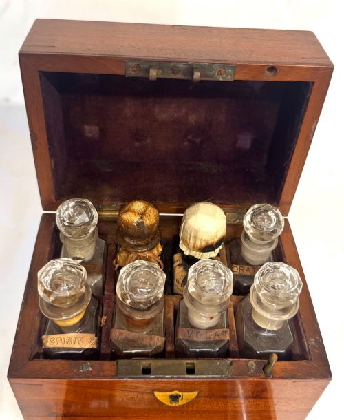 fig 2. An antique wooden apothecary box shown open with glass stoppered bottles in top compartments and labelled vials in a velvet-lined lower drawer.