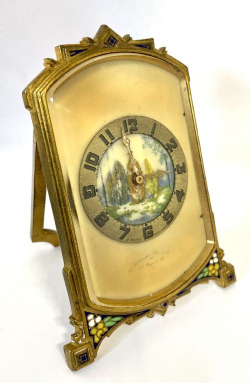 fig 1. An antique miniature gilt metal easel clock featuring a painted landscape dial surrounded by champleve enamel floral decoration at the base.
