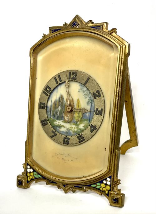 fig 2. An antique miniature gilt metal easel clock featuring a painted landscape dial surrounded by champleve enamel floral decoration at the base.