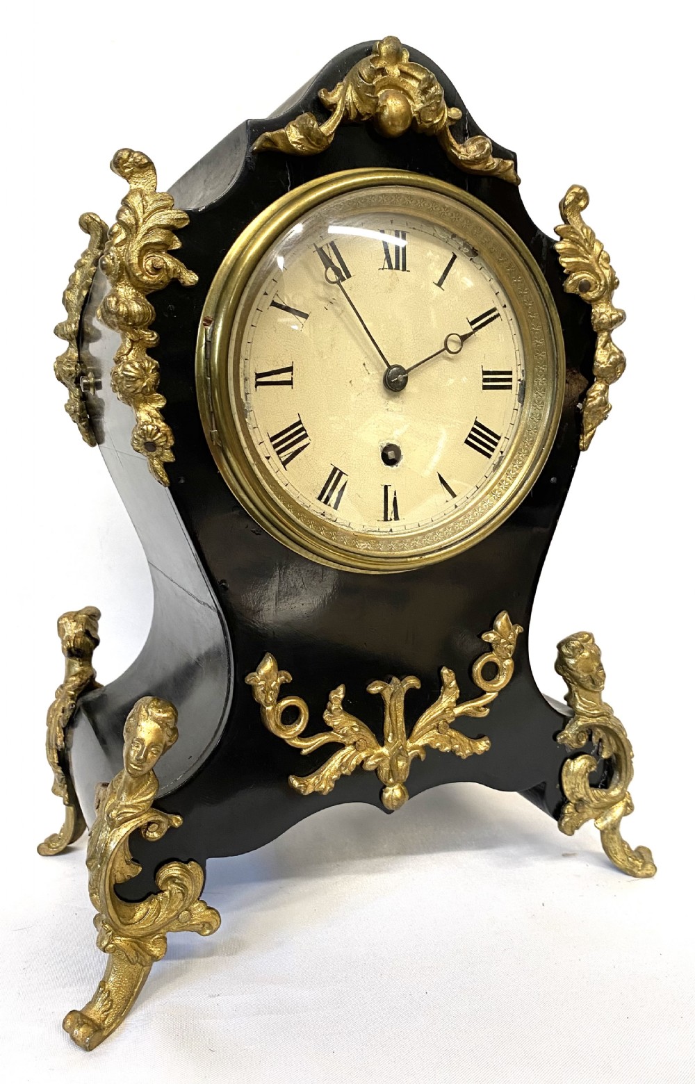 An antique ebonised wooden mantel clock featuring ornate cast ormolu mounts, a white dial with Roman numerals, and scrolled gilt brass feet.