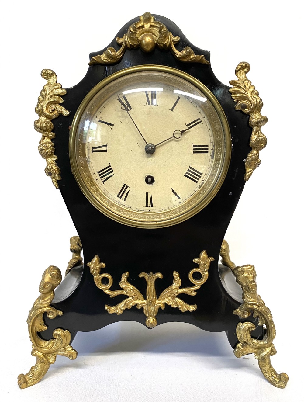 An antique ebonised wooden mantel clock featuring ornate cast ormolu mounts, a white dial with Roman numerals, and scrolled gilt brass feet. View II