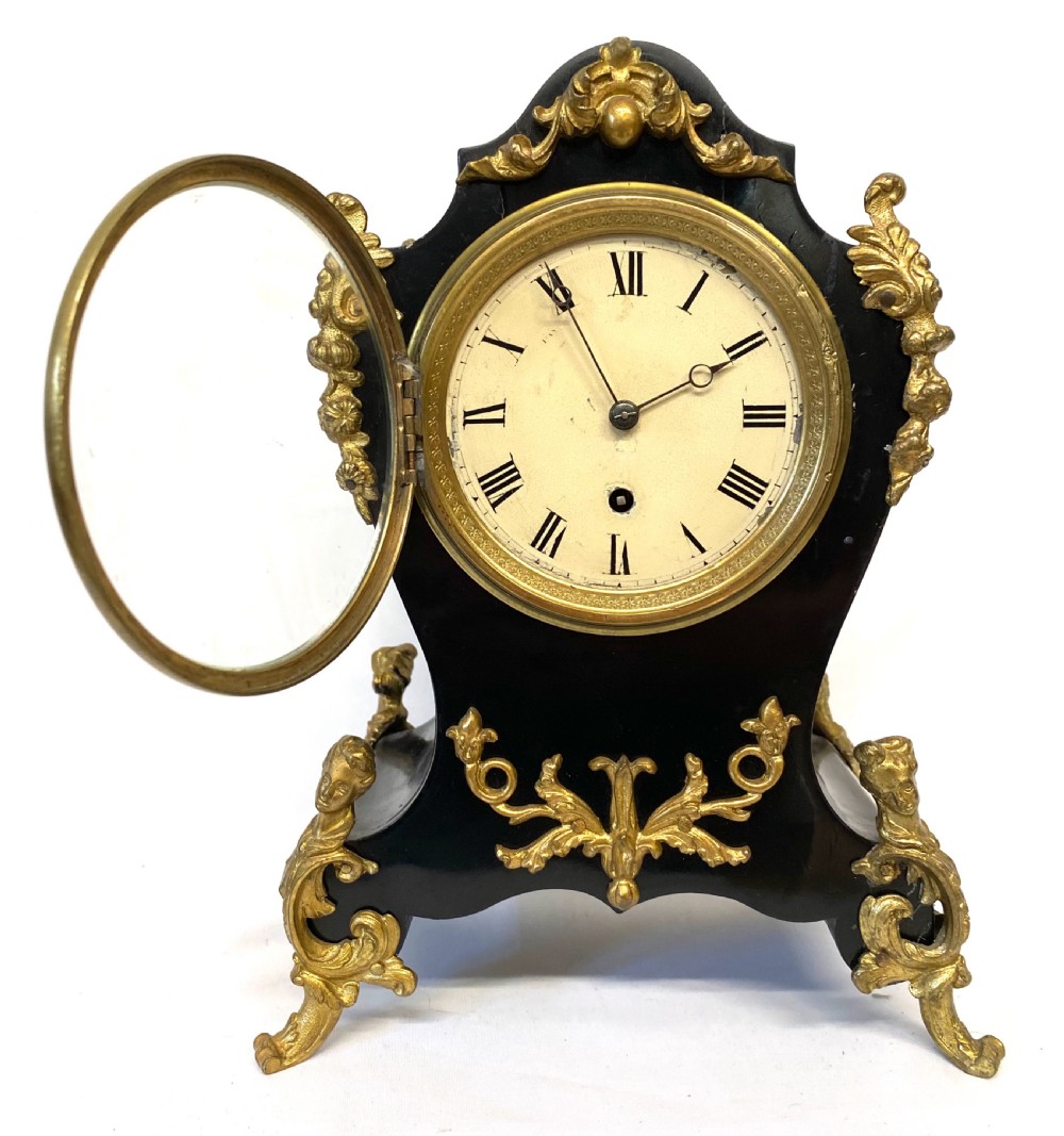 An antique ebonised wooden mantel clock featuring ornate cast ormolu mounts, a white dial with Roman numerals, and scrolled gilt brass feet. View III