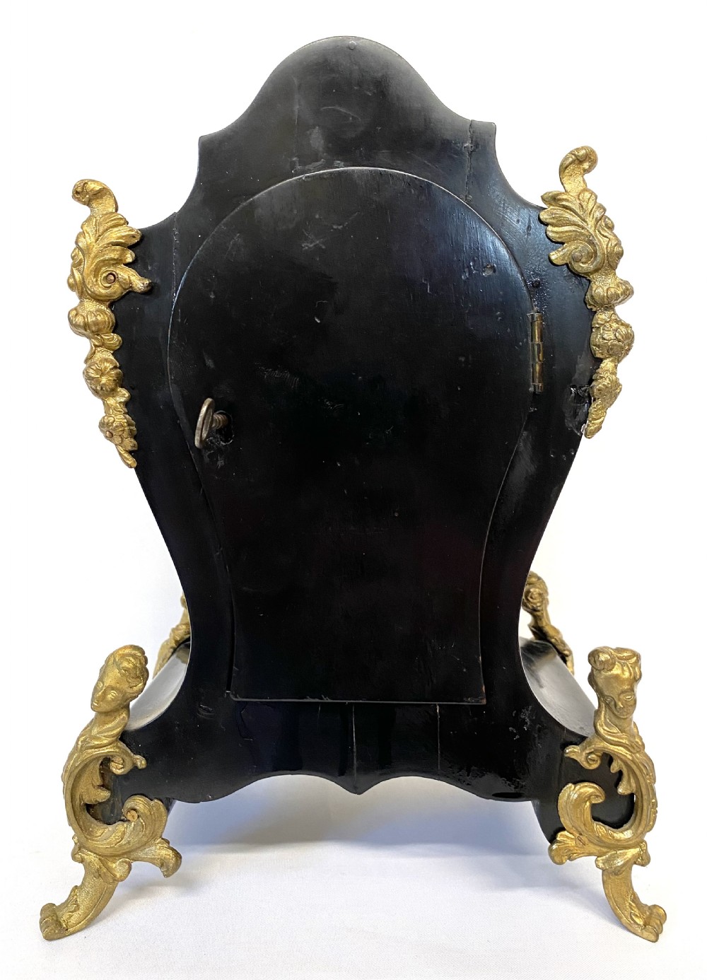 An antique ebonised wooden mantel clock featuring ornate cast ormolu mounts, a white dial with Roman numerals, and scrolled gilt brass feet. View IX